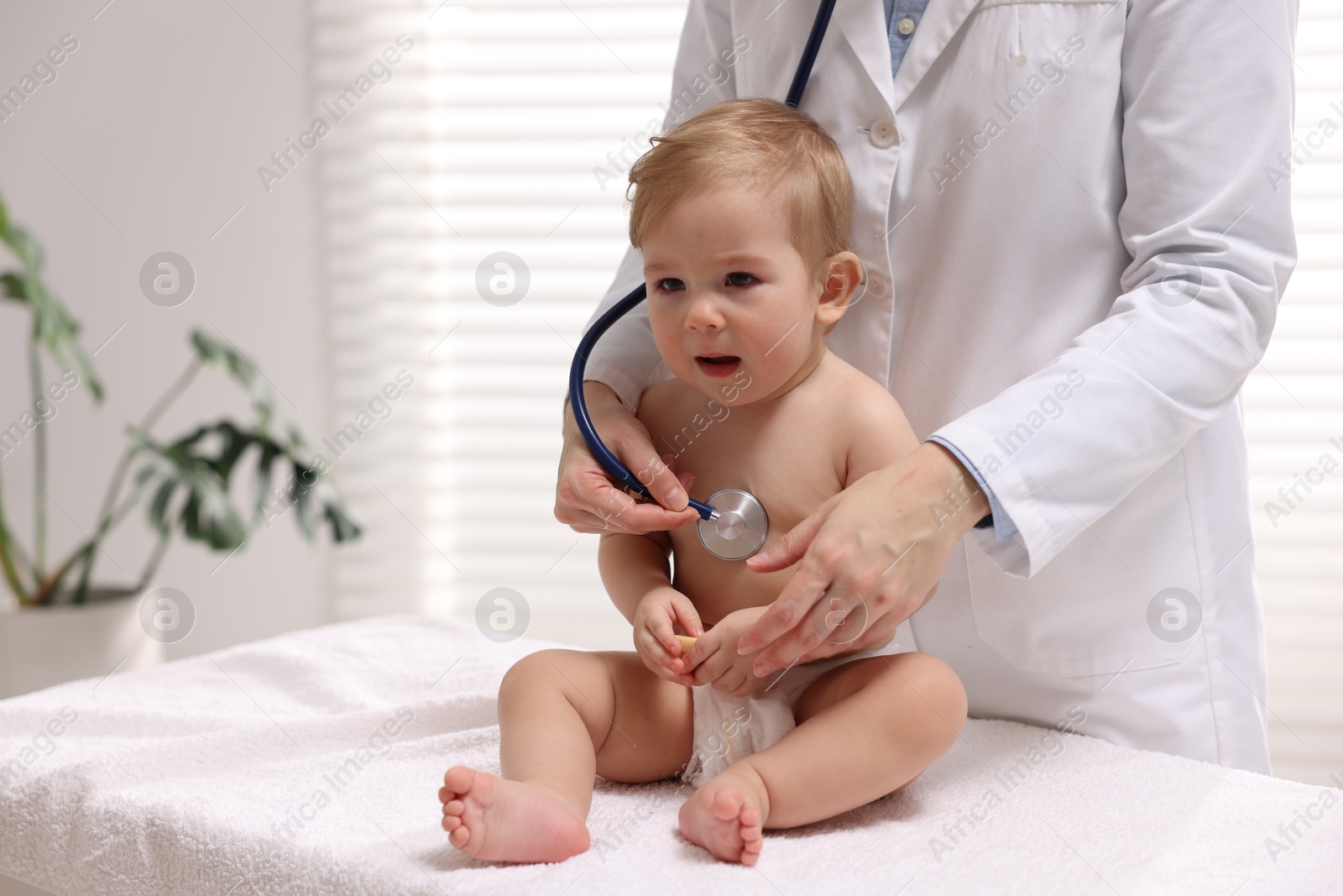 Photo of Pediatrician examining cute little baby in clinic, closeup