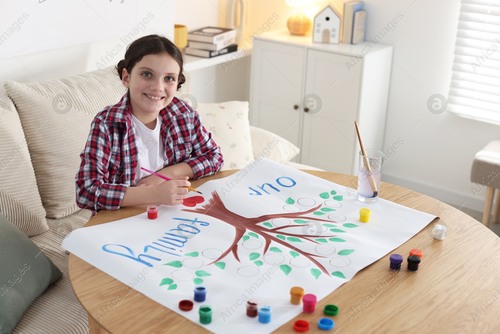 Photo of Girl drawing her family tree with paints at wooden table indoors