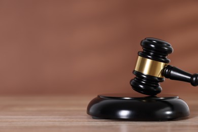 Photo of Judge's gavel and sound block on wooden table against brown background, closeup. Space for text