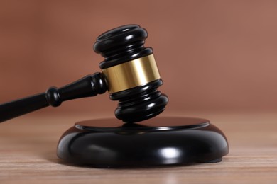 Photo of Judge's gavel and sound block on wooden table against brown background, closeup