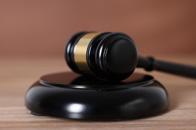 Photo of Judge's gavel and sound block on wooden table against brown background, closeup