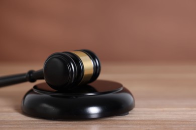 Photo of Judge's gavel and sound block on wooden table against brown background, closeup
