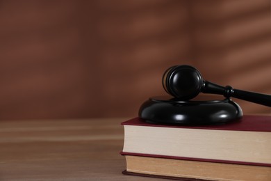 Photo of Judge's gavel, sound block and books on wooden table against brown background, closeup. Space for text