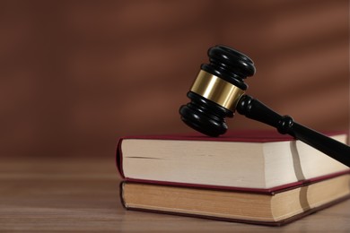 Photo of Judge's gavel and books on wooden table against brown background, closeup. Space for text