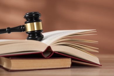 Photo of Judge's gavel and books on wooden table against brown background, closeup
