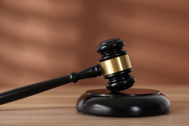 Photo of Judge's gavel and sound block on wooden table against brown background, closeup