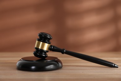 Photo of Judge's gavel and sound block on wooden table against brown background, closeup