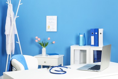 Photo of Doctor's workplace. Laptop and stethoscope on white table in medical office