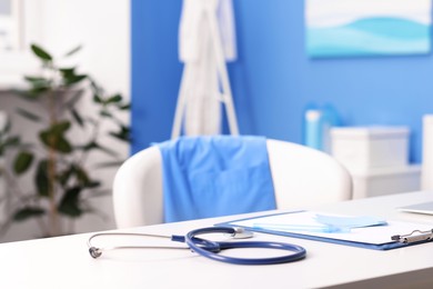 Photo of Doctor's workplace. Stethoscope, clipboard and pen on white table in medical office, closeup