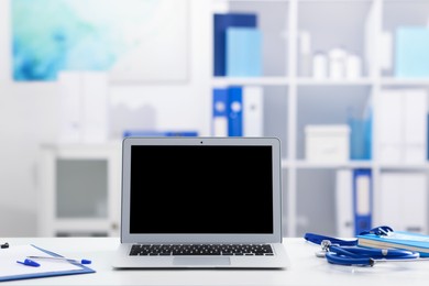 Photo of Doctor's workplace with stethoscope, paperwork and laptop on desk