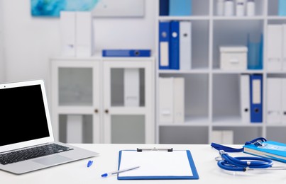 Photo of Doctor's workplace with stethoscope, paperwork and laptop on desk. Space for text