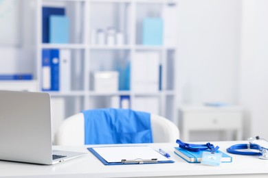 Photo of Doctor's workplace with stethoscope, paperwork and laptop on desk. Space for text