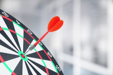 Image of Targeting and business success. Dart sticking in center of dartboard in office, closeup