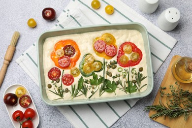 Photo of Raw focaccia with vegetables, spices and brush on light grey table, flat lay