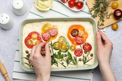 Photo of Woman adding thyme to raw focaccia at grey table, top view