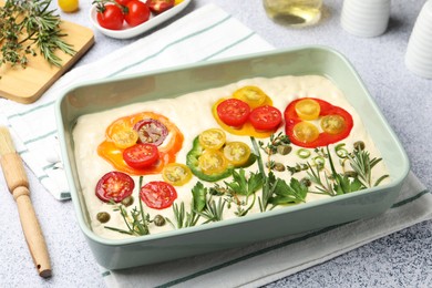 Photo of Raw focaccia with vegetables, spices and brush on light grey table, closeup
