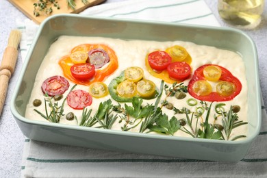 Photo of Raw focaccia with vegetables, spices and brush on light grey table, closeup