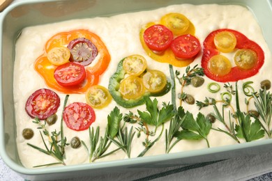 Photo of Raw focaccia with vegetables and spices in baking dish on table, above view