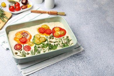 Photo of Raw focaccia with vegetables, spices and brush on light grey table, space for text
