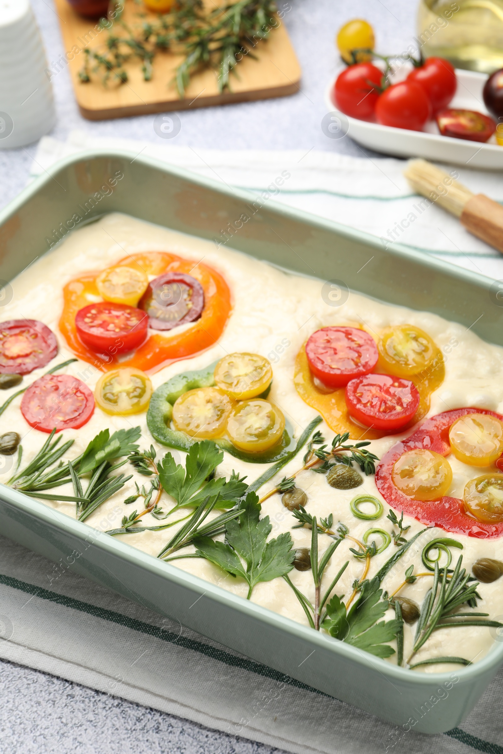Raw focaccia with vegetables, spices and brush on light grey table, closeup Photo of Raw focaccia with vegetables, spices and brush on light grey table, closeup