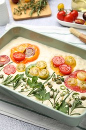 Photo of Raw focaccia with vegetables, spices and brush on light grey table, closeup