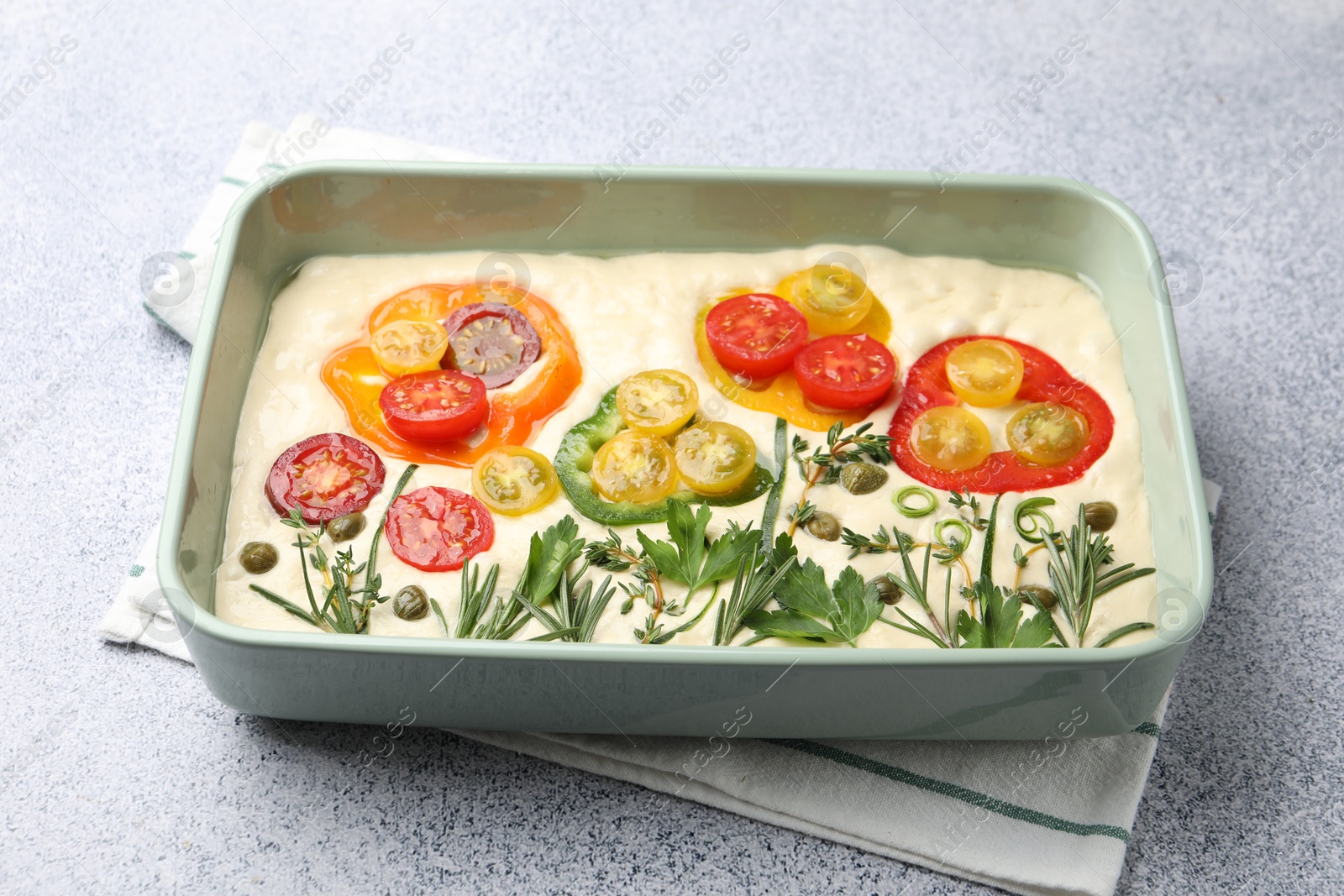 Raw focaccia with vegetables and spices in baking dish on light grey table, closeup Photo of Raw focaccia with vegetables and spices in baking dish on light grey table, closeup
