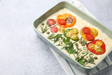 Photo of Raw focaccia with vegetables and spices in baking dish on light grey table, closeup. Space for text