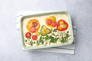 Photo of Raw focaccia with vegetables and spices in baking dish on light grey table, top view