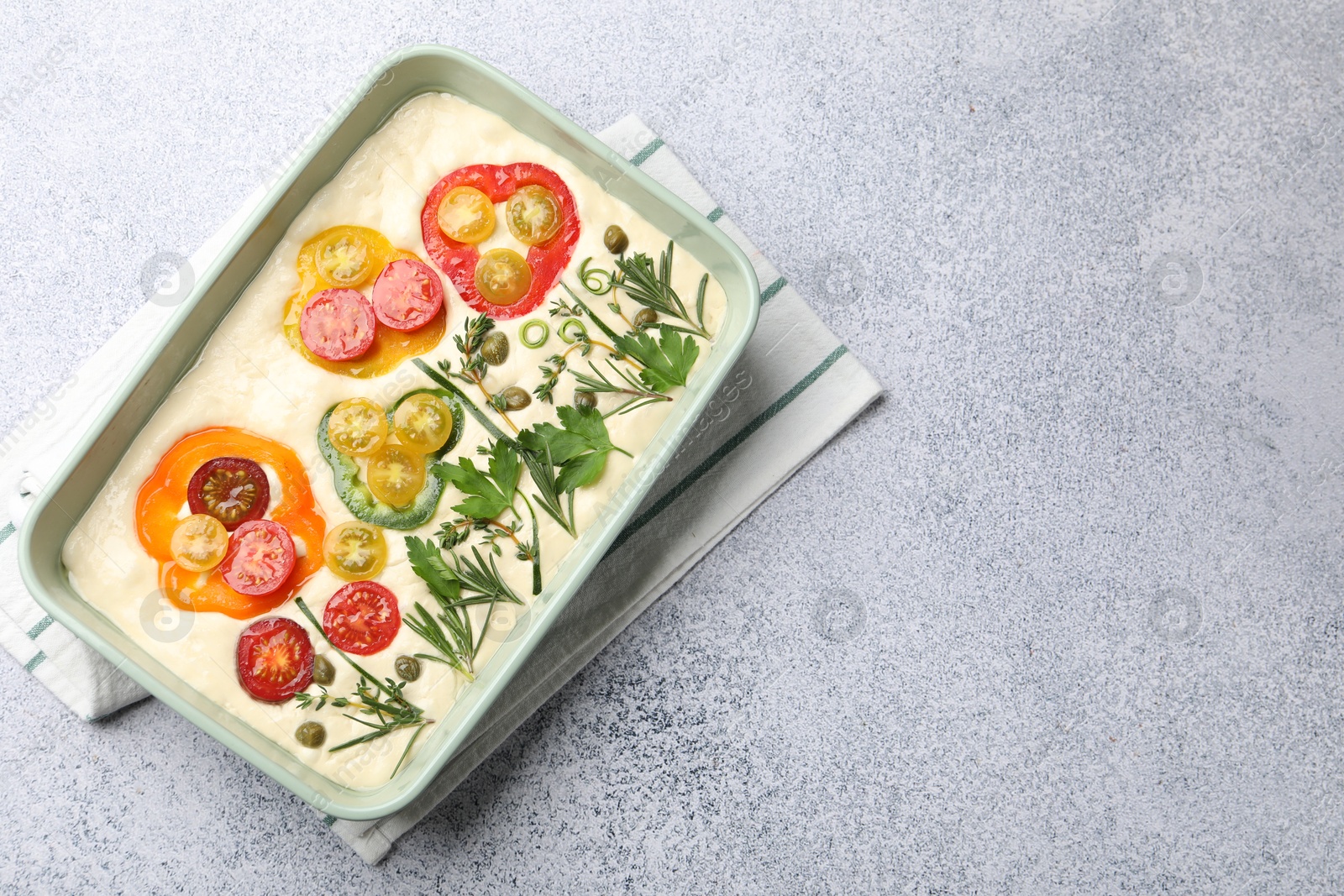 Raw focaccia with vegetables and spices in baking dish on light grey table, top view. Space for text Photo of Raw focaccia with vegetables and spices in baking dish on light grey table, top view. Space for text