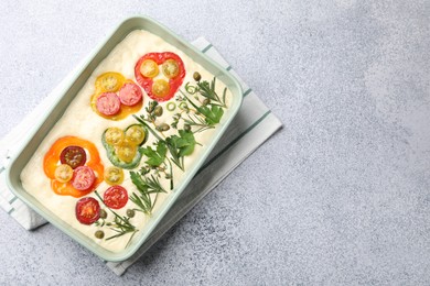Photo of Raw focaccia with vegetables and spices in baking dish on light grey table, top view. Space for text
