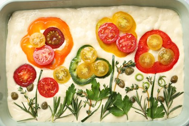 Photo of Raw focaccia with vegetables and spices in baking dish, top view