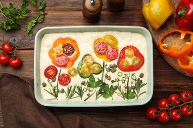 Photo of Raw focaccia with vegetables and spices on wooden table, flat lay