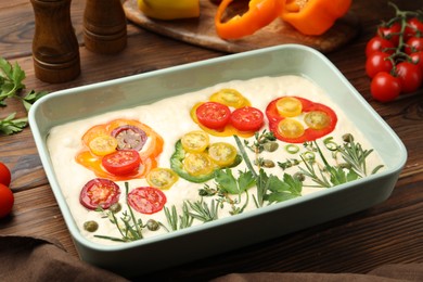 Photo of Raw focaccia with vegetables and spices on wooden table, closeup