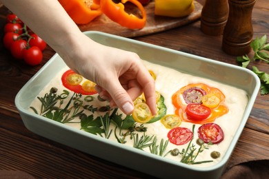 Photo of Woman adding tomato to raw focaccia at wooden table, closeup
