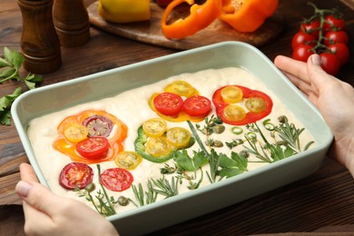 Photo of Woman with raw focaccia and ingredients at wooden table, closeup