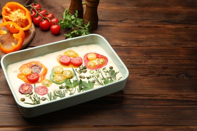 Photo of Raw focaccia with vegetables and spices on wooden table, closeup. Space for text