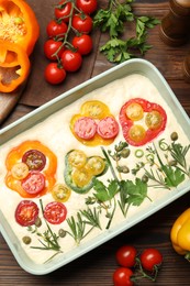 Photo of Raw focaccia with vegetables and spices on wooden table, flat lay