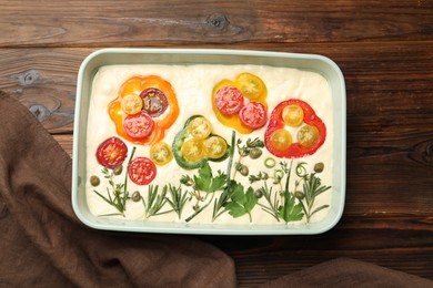 Photo of Raw focaccia with vegetables and spices in baking dish on wooden table, top view