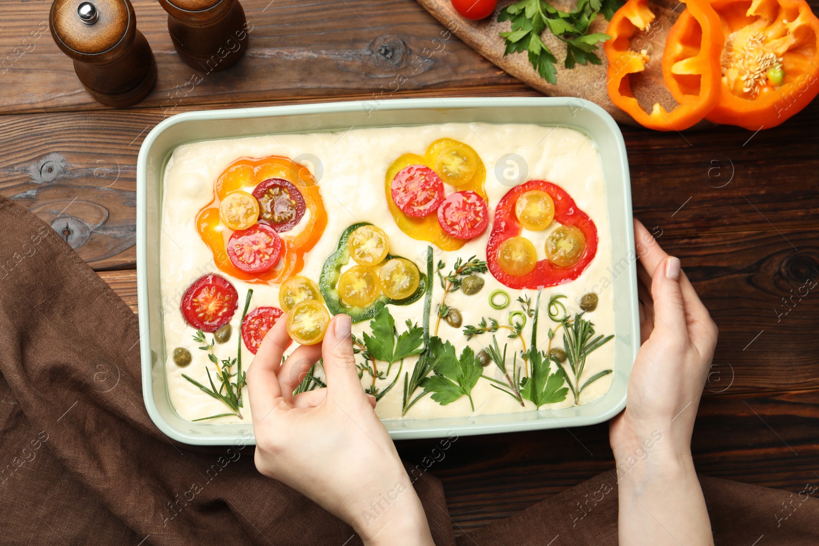 Woman adding tomato to raw focaccia at wooden table, top view Photo of Woman adding tomato to raw focaccia at wooden table, top view