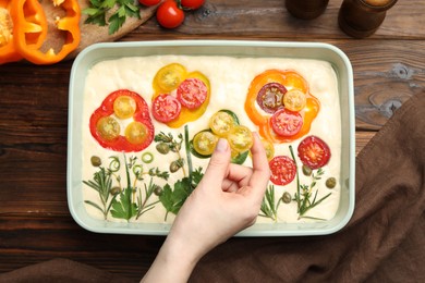 Photo of Woman adding tomato to raw focaccia at wooden table, top view