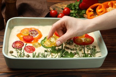 Photo of Woman adding tomato to raw focaccia at wooden table, closeup