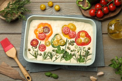 Photo of Raw focaccia with vegetables, spices and brush on wooden table, flat lay