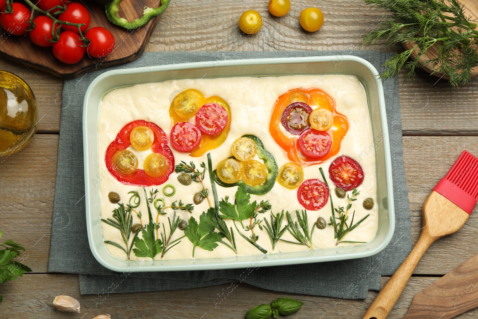 Raw focaccia with vegetables, spices and brush on wooden table, flat lay Photo of Raw focaccia with vegetables, spices and brush on wooden table, flat lay
