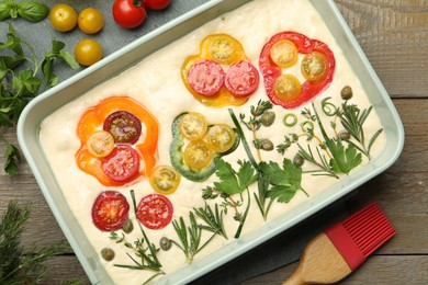 Photo of Raw focaccia with vegetables, spices and brush on wooden table, flat lay