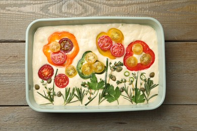Photo of Raw focaccia with vegetables and spices in baking dish on wooden table, top view