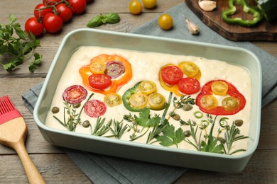 Photo of Raw focaccia with vegetables, spices and brush on wooden table, closeup