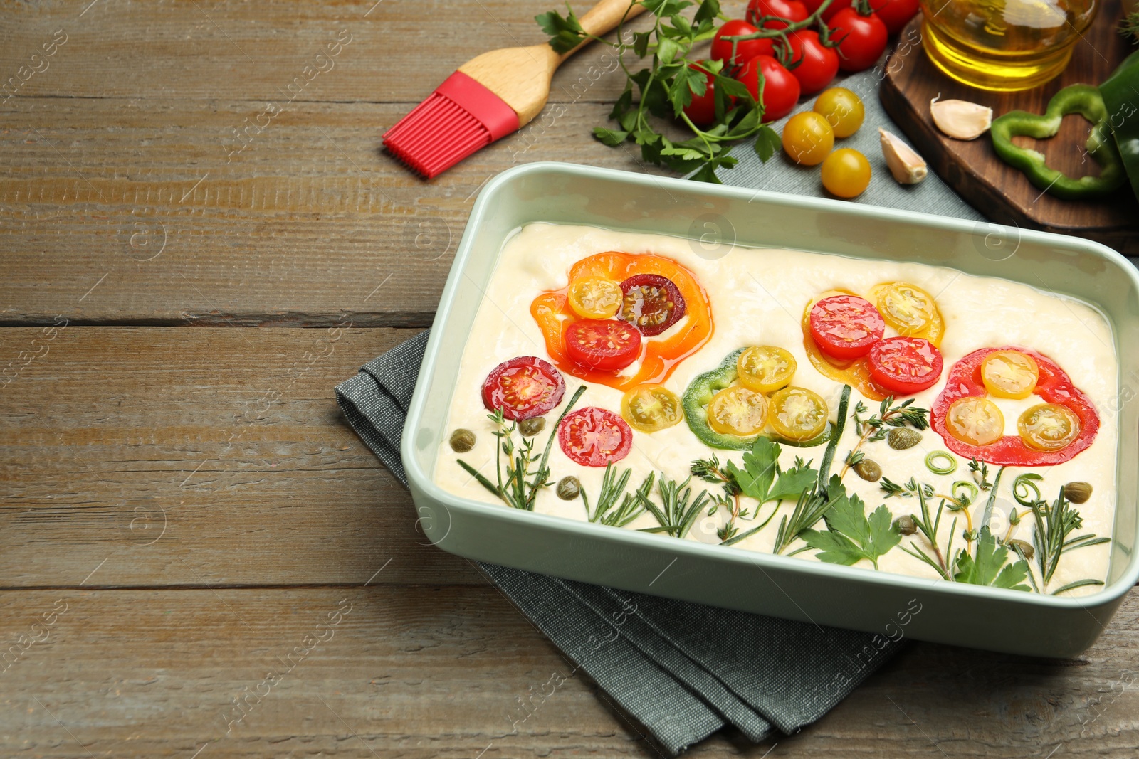 Raw focaccia with vegetables, spices and brush on wooden table, closeup. Space for text Photo of Raw focaccia with vegetables, spices and brush on wooden table, closeup. Space for text