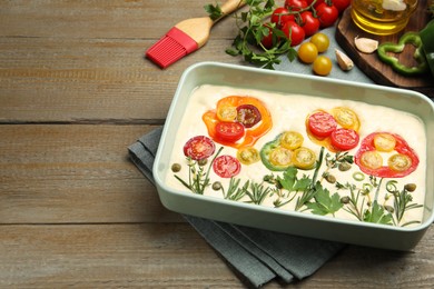 Photo of Raw focaccia with vegetables, spices and brush on wooden table, closeup. Space for text