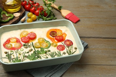 Photo of Raw focaccia with vegetables, spices and brush on wooden table, closeup. Space for text