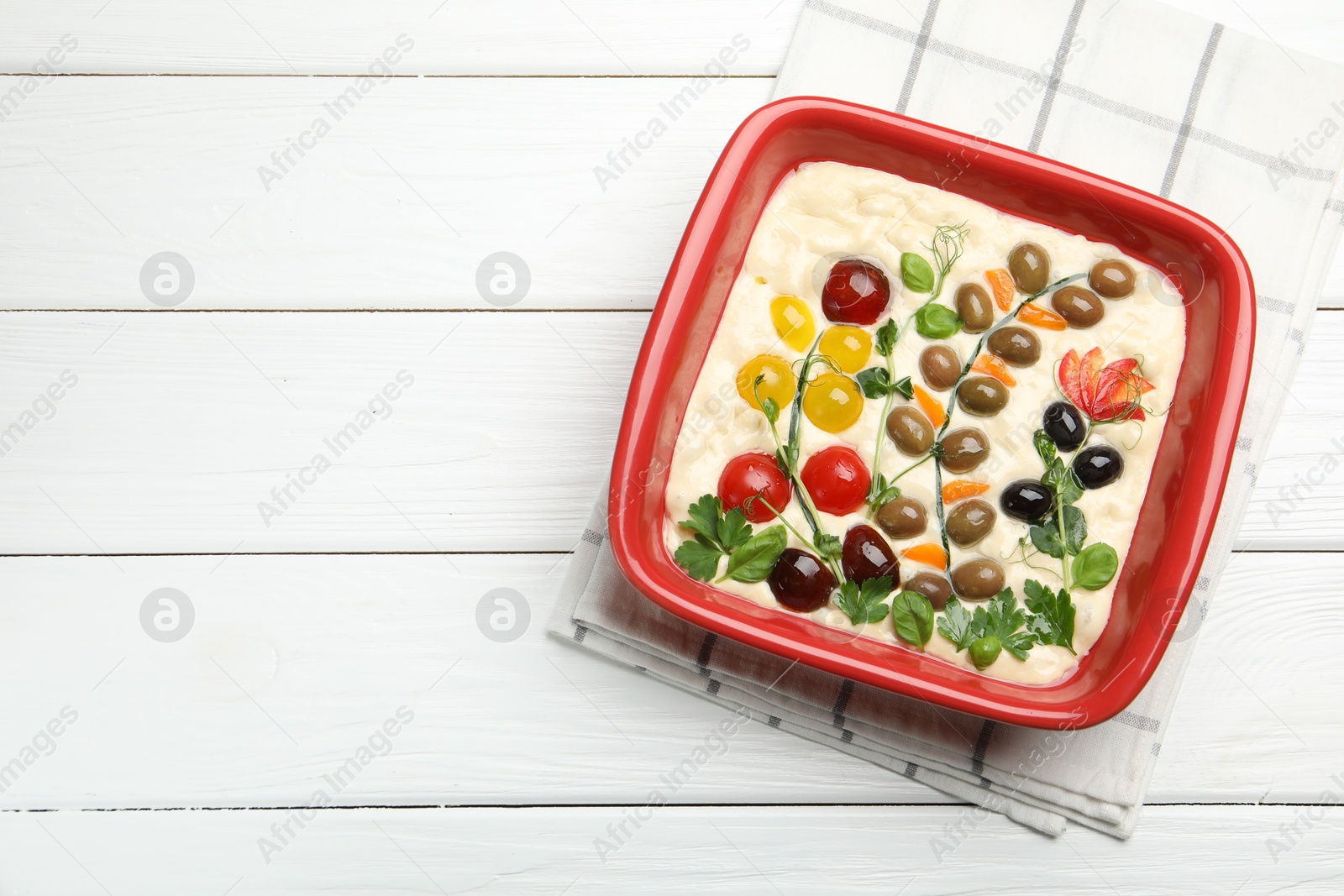 Raw focaccia with vegetables and olives in baking dish on white wooden table, top view. Space for text Photo of Raw focaccia with vegetables and olives in baking dish on white wooden table, top view. Space for text